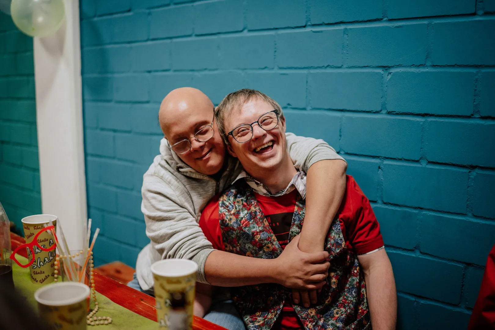 Zwei Personen sitzen eng beieinander und lachen herzlich, während eine Person die andere freundschaftlich umarmt.