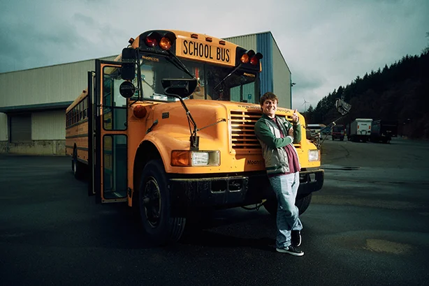 Person lehnt lässig an einem gelben Schulbus auf einem Parkplatz