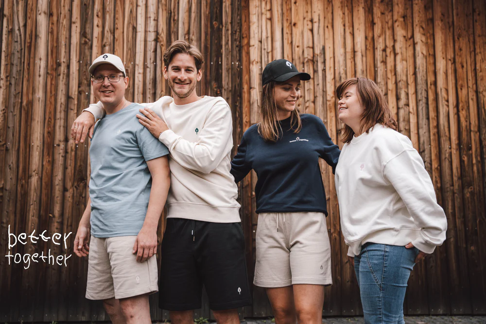 Vier Personen in Freizeitkleidung stehen lachend zusammen vor einer hölzernen Wand.