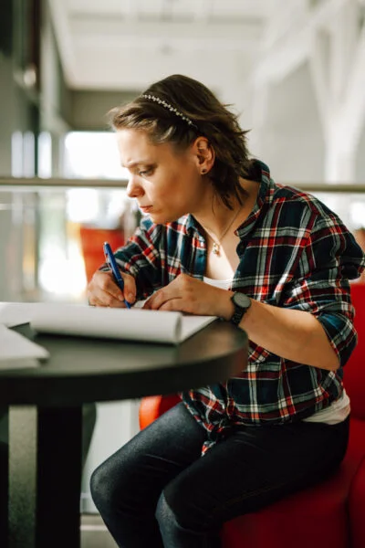 Person sitzt an einem Tisch und schreibt konzentriert in ein Heft.